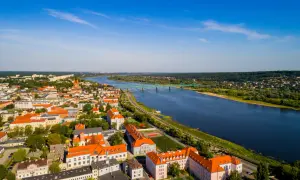 Widok z lotu ptaka na miasto nad Wisłą, z zielonym mostem i zabudowaniami o pomarańczowych dachach.