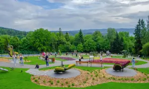Kolorowy park z rzeźbami z kwiatów i ludźmi spacerującymi po alejkach. W oddali widać zalesione wzgórza. Ile się idzie, tyle piękna!