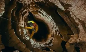 Speleolog w żółtym kombinezonie zjazduje w głąb skalnej otchłani, eksplorując potencjalnie najgłębszą jaskinię na świecie.