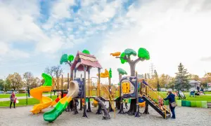Kolorowy plac zabaw w Krakowie z wieloma zjeżdżalniami i elementami do wspinaczki. Dzieci bawią się wesoło pod błękitnym niebem.