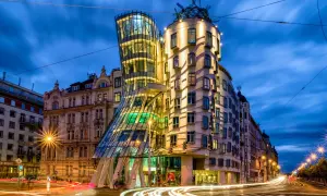 Tańczący dom w Pradze, nocą, z rozmazanymi światłami samochodów na ulicy.