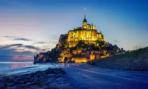 Mont Saint-Michel, jeden z najpiękniejszych zamków w Europie, lśni w blasku wieczornych świateł na tle błękitnego nieba.