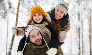 Rodzina cieszy się zimową atmosferą. Ojciec niesie córkę na barana, mama obejmuje ich. To wspaniałe kołobrzeg atrakcje zimą!