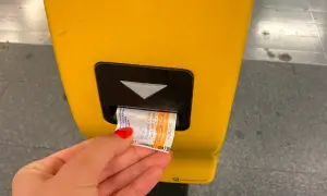 Ręka z czerwoną hybrydą wkłada bilet do żółtego automatu. Praga komunikacja miejska to wygoda podróżowania.