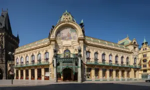 Reprezentacyjny miejski dom w Pradze, z bogatą mozaiką i kopułą, sąsiaduje z gotycką wieżą.