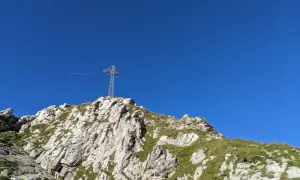 Giewont, śpiący rycerz, wznosi się ku błękitnemu niebu. Na szczycie stoi krzyż, a pod nim skaliste zbocza porośnięte trawą.