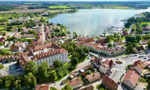 Malownicze miasteczko nad jeziorem, gdzie białe budynki z czerwonymi dachami tworzą urokliwy krajobraz. To prawdziwa kraina tysiąca jezior, pełna zieleni i spokoju.