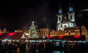 Tłum ludzi na jarmarku bożonarodzeniowym w Pradze, w tle iluminowana choinka i zabytkowe budynki.