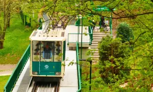 Kolejka linowa Praga w zieleni. Wagonik z numerem 1 zbliża się do stacji, otoczony bujną roślinnością.