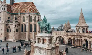 Budapeszt stare miasto: Rycerz na koniu przed kościołem z kolorowym dachem i basztami. Turyści spacerują po brukowanym placu.