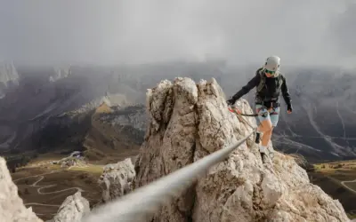 Kobieta na via ferrata polska pokonuje skalną grań, w tle górzysty krajobraz z krętymi drogami.
