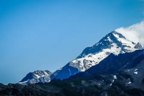 Majestatyczne szczyty Alp, pokryte śniegiem, z chmurami otulającymi wierzchołek. Widok na wejście na Mont Blanc.