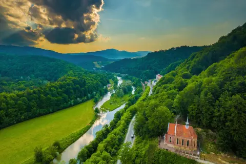 Malownicze **Beskid Sądecki szlaki** wiodą przez zielone doliny, wzdłuż rzeki i lasów, z widokiem na urokliwy kościółek.