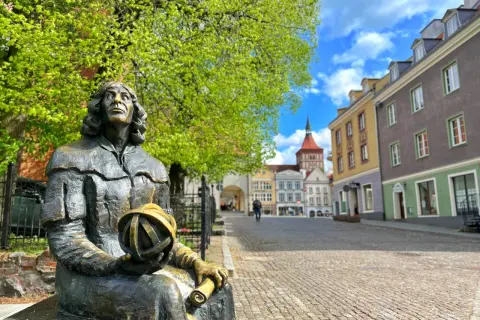 Pomnik Kopernika, jeden z olsztyn atrakcje turystyczne, siedzi na tle kolorowych kamienic i błękitnego nieba.