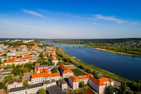 Widok z lotu ptaka na miasto nad Wisłą, z zielonym mostem i zabudowaniami o pomarańczowych dachach.