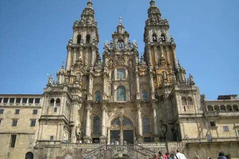 Majestatyczna katedra w Santiago de Compostela z trzema wieżami i schodami, po których wchodzą pielgrzymi.