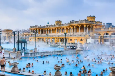 Ludzie kąpią się w gorących źródłach, które są jednymi z najlepszych term w Europie, z piękną, żółtą architekturą w tle.