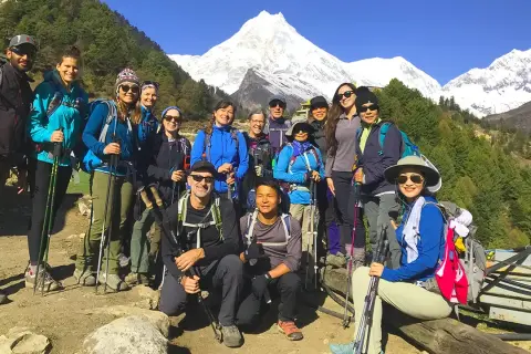 Grupa turystów z plecakami i kijkami trekkingowymi pozuje na tle ośnieżonych gór podczas Manaslu Circuit Trek.