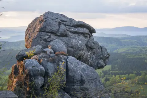Skalny labirynt na trasie w Górach Stołowych. Majestatyczne formacje skalne na tle zielonych wzgórz i nieba.