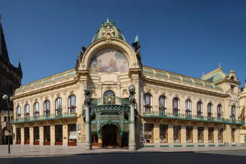 Reprezentacyjny miejski dom w Pradze, z bogatą mozaiką i kopułą, sąsiaduje z gotycką wieżą.