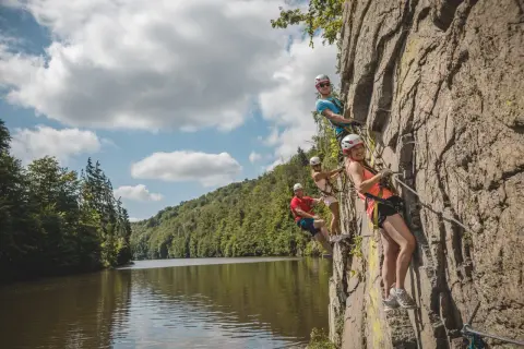 Grupa przyjaciół pokonuje via ferrata w Czechach, wspinając się po skalnej ścianie nad malowniczą rzeką.