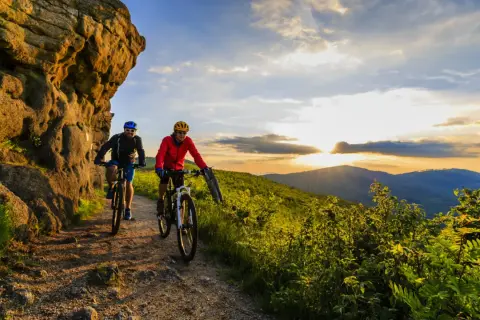 Dwóch rowerzystów przemierza malownicze trasy rowerowe w Polsce, podziwiając zachód słońca nad wzgórzami.
