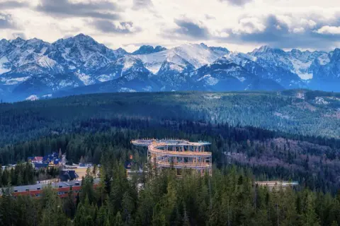 Drewniana wieża widokowa w Zakopanem wznosi się pośród lasów, oferując zapierający dech w piersiach widok na ośnieżone Tatry.