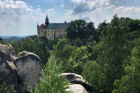 Zamek Hrubá Skála wznosi się dumnie nad skalistym krajobrazem, otoczony bujną zielenią drzew.