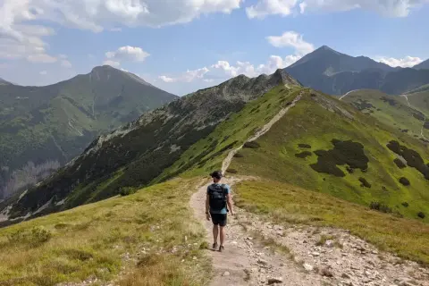 Wędrowiec na szlaku na Ornaka z Doliny Kościeliskiej. Zielone zbocza górskie, kamienista ścieżka i błękitne niebo z chmurami.