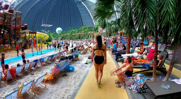 Tropikalny raj w aquaparku pod Berlinem. Ludzie odpoczywają na plaży pod ogromną kopułą, wśród palm i zjeżdżalni.