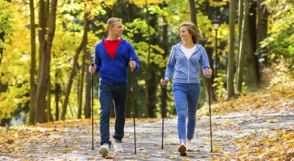 Para spaceruje po jesiennym parku, uprawiając nordic walking. Liście tworzą kolorowy dywan.