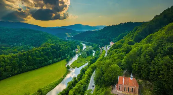Malownicze **Beskid Sądecki szlaki** wiodą przez zielone doliny, wzdłuż rzeki i lasów, z widokiem na urokliwy kościółek.