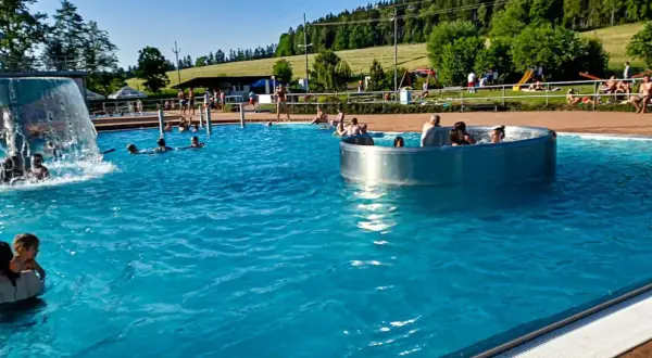 Słoneczny dzień na basenie w Czechach, blisko granicy. Ludzie kąpią się i relaksują w wodzie, ciesząc się wakacjami.