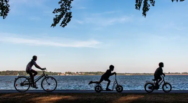 Dzieci na rowerach i hulajnogach przemierzają malownicze rowy trasy rowerowe nad jeziorem.