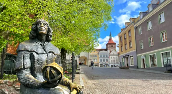 Pomnik Kopernika, jeden z olsztyn atrakcje turystyczne, siedzi na tle kolorowych kamienic i błękitnego nieba.