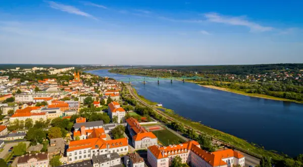 Widok z lotu ptaka na miasto nad Wisłą, z zielonym mostem i zabudowaniami o pomarańczowych dachach.