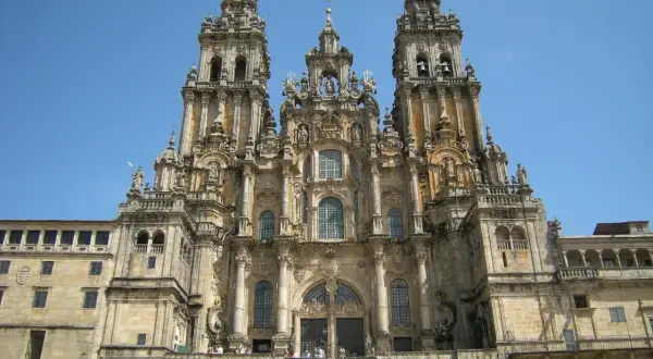 Majestatyczna katedra w Santiago de Compostela z trzema wieżami i schodami, po których wchodzą pielgrzymi.