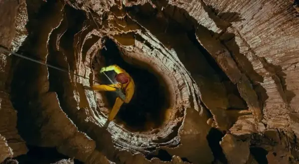 Speleolog w żółtym kombinezonie zjazduje w głąb skalnej otchłani, eksplorując potencjalnie najgłębszą jaskinię na świecie.