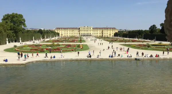 Wiedeń: Pałac Schönbrunn i jego ogrody, gdzie turyści spacerują pośród kwiatowych rabat i podziwiają architekturę.