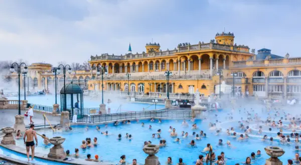 Ludzie kąpią się w gorących źródłach, które są jednymi z najlepszych term w Europie, z piękną, żółtą architekturą w tle.