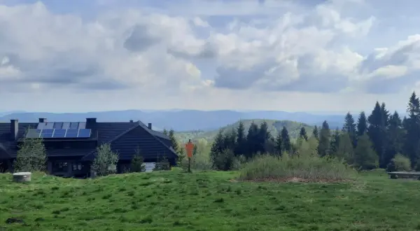 Dom z panelami słonecznymi na tle gór i lasów. Widok na szlaki Jaworzyny Krynickiej.