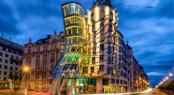 Tańczący dom w Pradze, nocą, z rozmazanymi światłami samochodów na ulicy.