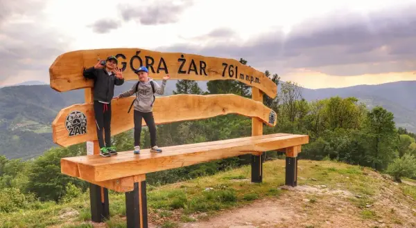 Dzieci pozują na ławce na szczycie Góry Żar (761 m n.p.m.), ciesząc się widokiem i trasą.