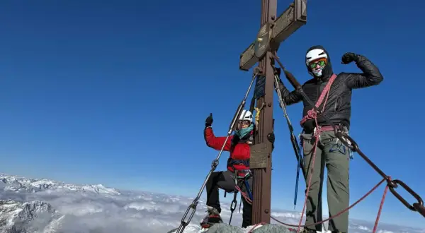 Dwóch alpinistów na szczycie Grossglockner, najwyższy szczyt Austrii. W tle morze chmur i ośnieżone góry.