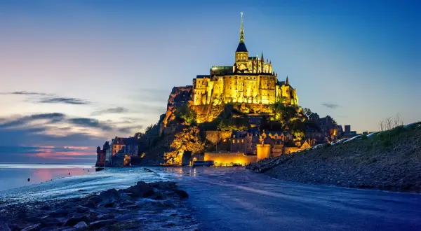 Mont Saint-Michel, jeden z najpiękniejszych zamków w Europie, lśni w blasku wieczornych świateł na tle błękitnego nieba.