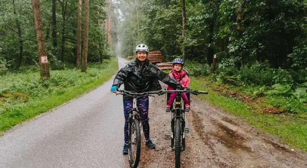 Mama i dziecko na rowerach w deszczu, odkrywają lasy kozłowieckie trasy rowerowe.