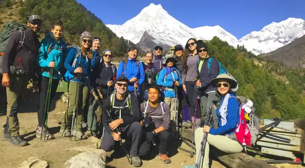 Grupa turystów z plecakami i kijkami trekkingowymi pozuje na tle ośnieżonych gór podczas Manaslu Circuit Trek.