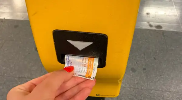 Ręka z czerwoną hybrydą wkłada bilet do żółtego automatu. Praga komunikacja miejska to wygoda podróżowania.