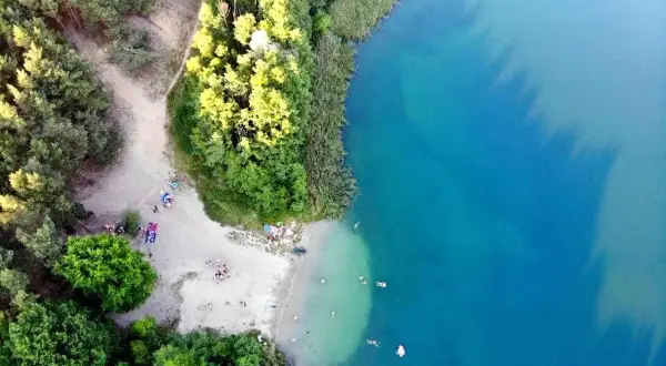Plaża nad jeziorem tętni życiem. Ludzie odpoczywają na piasku, kąpią się w krystalicznie czystej wodzie, ciesząc się letnim dniem.