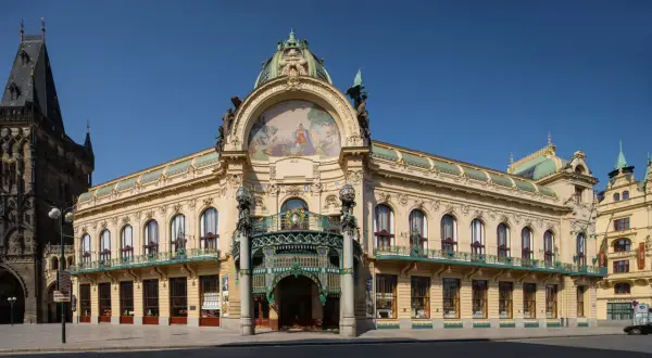 Reprezentacyjny miejski dom w Pradze, z bogatą mozaiką i kopułą, sąsiaduje z gotycką wieżą.